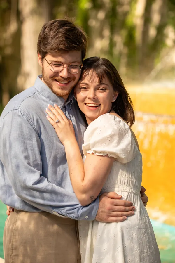 The couple holding each other and laughing, a fountain behind them