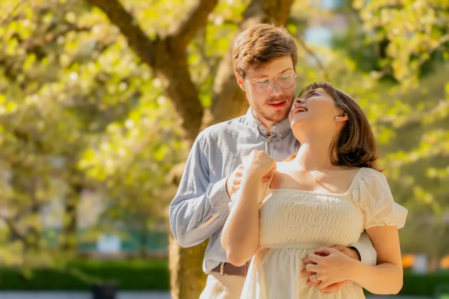 She tips her head back laughing while he holds her under a tree