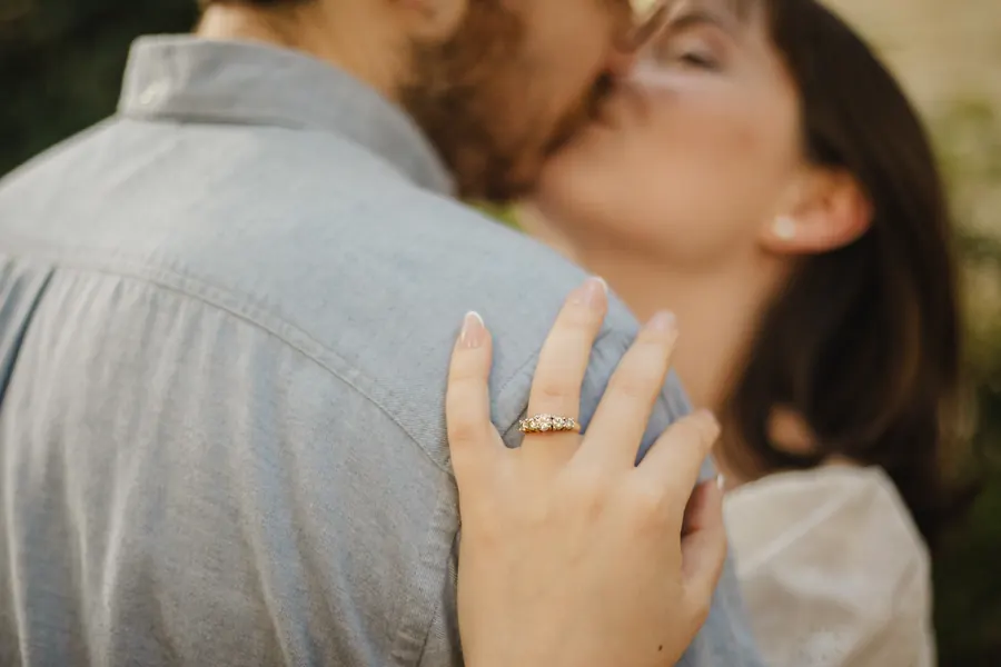 Close on her hand and the engagement ring as they kiss