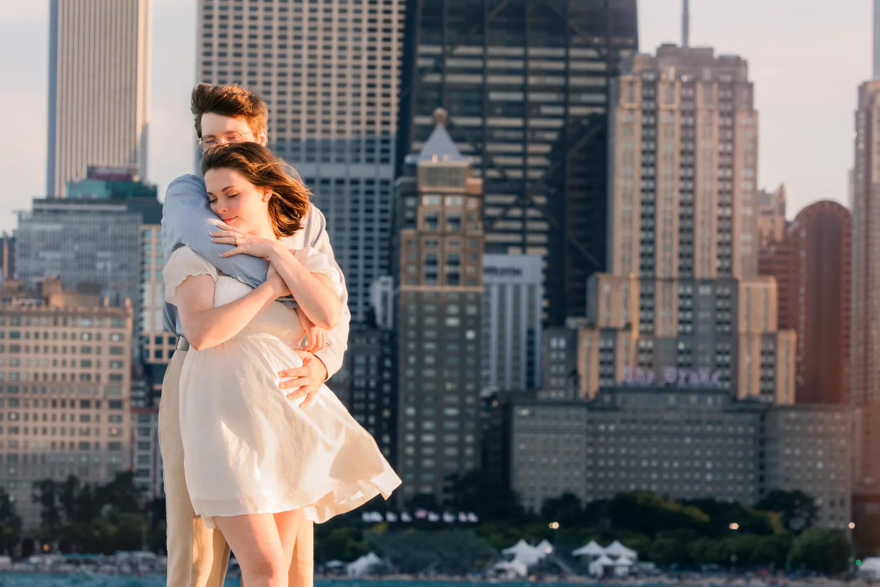 The couple on the Chicago lakefront at golden hour, the skyline rising behind them