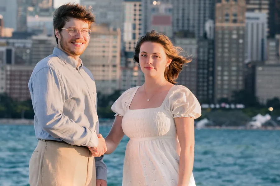 The couple standing hand in hand, her hair lifting in the wind